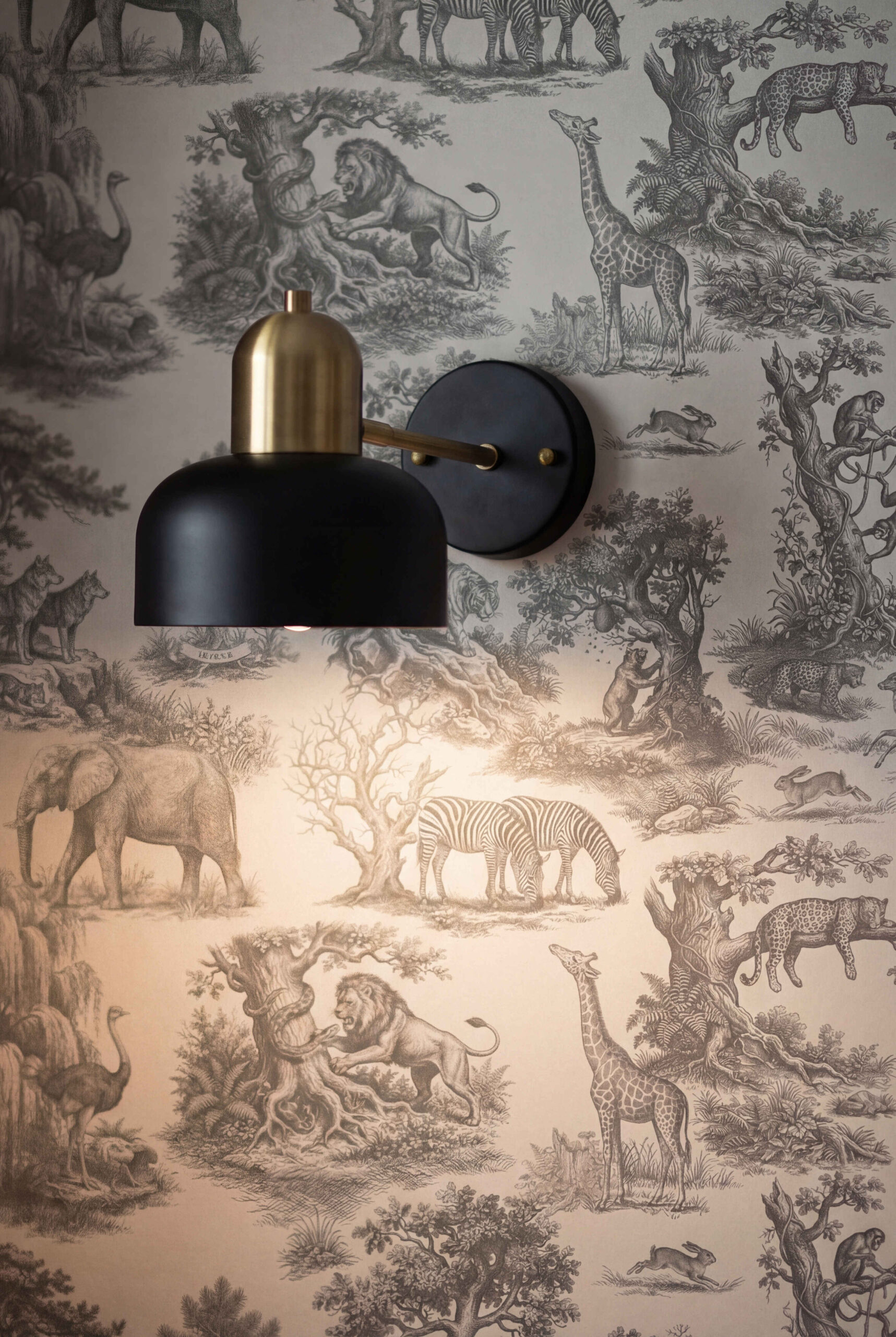 Musee | Wilderness Toile Wallpaper Classic Toile de Jouy wallpaper by Musee featuring intricate engravings of wild animals like giraffes, elephants, lions, and monkeys amidst trees and nature.